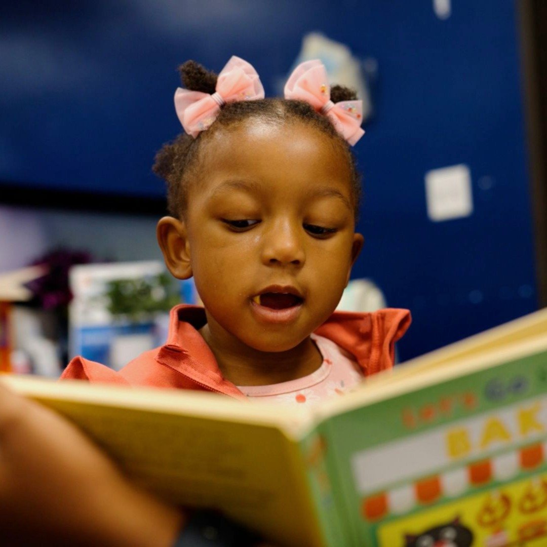Young girl with pink hair bows practicing reading a book